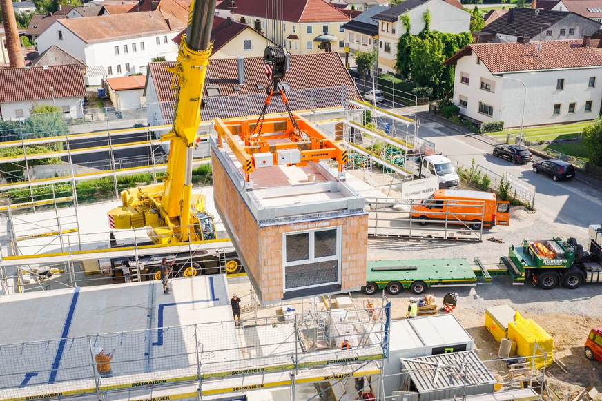 Auf der Baustelle hievt ein Kran die Module auf ihren Platz, wo sie mit anderen verbunden werden und in Kürze bezugsfertig sind.