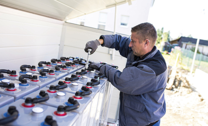 Ein Monteur installiert in einem energieautarken Einfamilien­haus einen Blei-Gel-Speicher, der auch das familieneigene Elektroauto lädt.