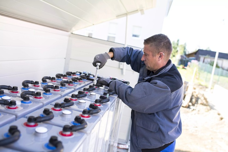 Ein Monteur installiert in einem energieautarken Einfamilien­haus einen Blei-Gel-Speicher, der auch das familieneigene Elektroauto lädt. - © BSW/Bormann
