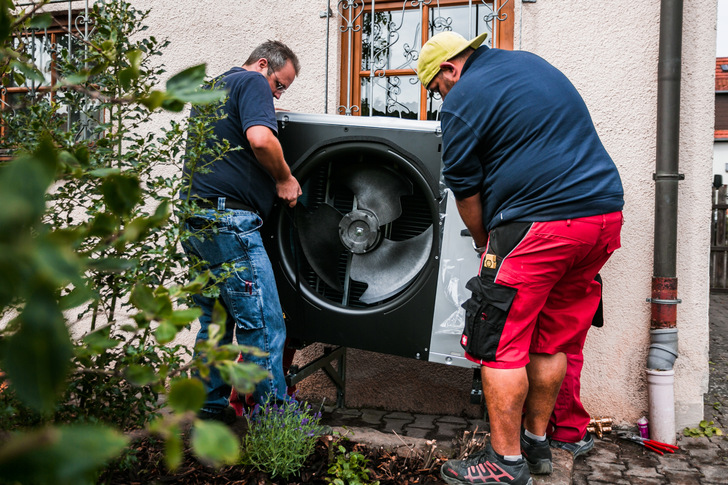 Die Heizungsmonteure stellen das Außengerät der Wärmepumpe auf die Wandhalterung.