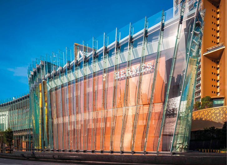 Eine im gleichen Winkel geneigte, durchgehende Innenfassade aus bronzen lackiertem Metallgewebe von GKD verleiht dem Hermès-Flagship- Store sowie der Fassade der Mega-Mall in Bangkok besonderen Glanz.