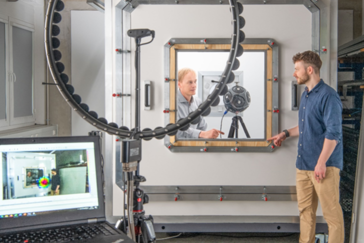 Luftdichtigkeitsmessung am Prüfstand ATLAS: Der kugelförmige Lautsprecher emittiert Schall, der durch Undichtigkeiten wie Löcher und Ritze, nach außen treten kann. Die außenstehende akustische Kamera kann durch die ringförmig angeordneten Mikrofone die Position von Schallquellen orten und analysieren. Der Ort des Schallaustritts – auf dem Computerbildschirm rot markiert – deutet auf eine Undichtigkeit in der Ecke des Fensters hin.