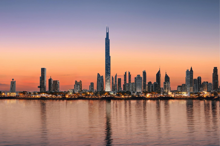 Skyline von Dubai bei Sonnenuntergang mit Wolkenkratzern, darunter der Burj Khalifa, die sich im ruhigen Wasser spiegeln. - © Azizi Developments, Duba