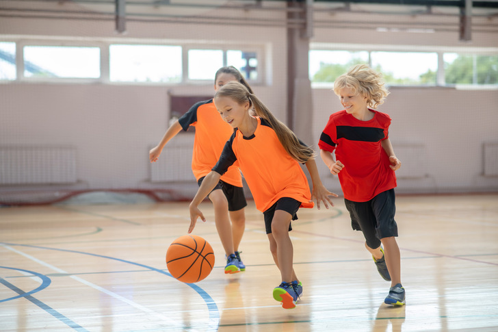 Drei Kinder spielen in einer Halle Basketball, wobei eines den Ball dribbelt und zwei andere ihm hinterherlaufen. - © zinkevych - stock.adobe.com