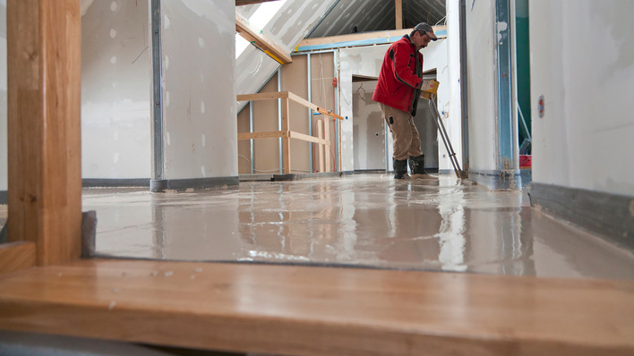 Funktioniert auch bei Sanierungen: Ein Handwerker verteilt flüssigen Estrich über der Flächenheizung.