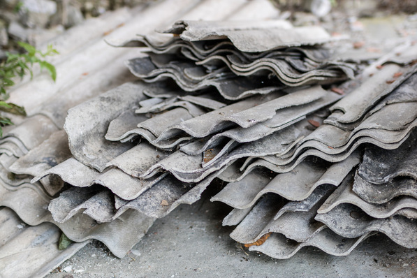 Alt-Text: „Stack von verwitterten, gewellten Asbestplatten auf einer Baustelle für Gebäude- und Anlagentechnik, die mögliche Gefahren bei unsachgemäßer Entsorgung verdeutlichen.“. - © Piotr - stock.adobe.com