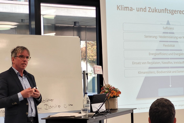 Person, die im Unterrichtsraum mit einer Folie und Notizen einen Vortrag zum Thema Klima und Zukunftsvorsorge hält. - © LNB - Leitfaden Nachhaltig Bauen