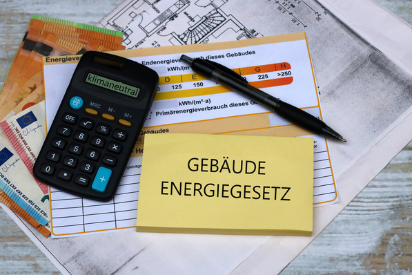 Taschenrechner, Stift und Dokumente mit dem deutschen Text „Gebäudeenergiegesetz“. Euroscheine und Architekturpläne sichtbar. - © Racamani - stock.adobe.com