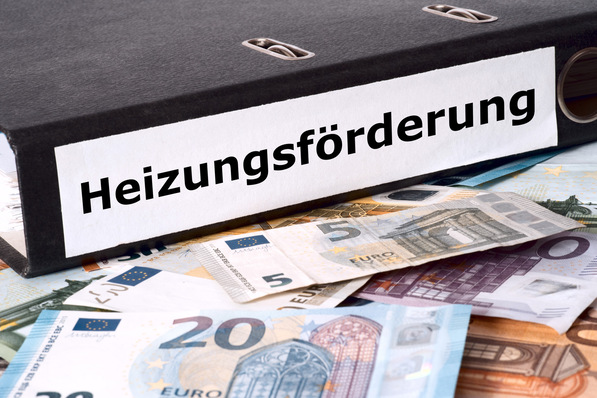 Ordner mit der Aufschrift „Heizungsförderung“ auf einem Tisch mit verschiedenen Euro-Banknoten. - © studio v-zwoelf - stock.adobe.com