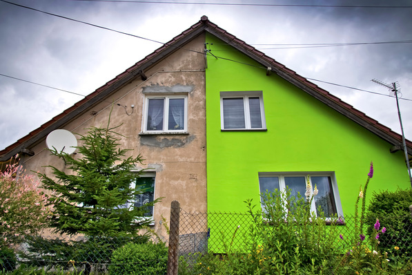 Ein Haus, dessen eine Hälfte hellgrün und dessen andere Hälfte abgenutzt und beige gestrichen ist, mit einem Garten davor. - © Tom Bayer - stock.adobe.com