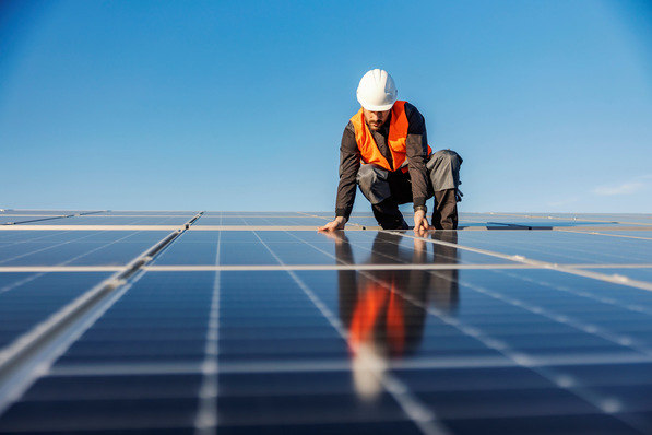 Arbeiter in Sicherheitsausrüstung installiert unter einem klaren blauen Himmel Solarmodule auf einem Dach. - © dusanpetkovic1 - stock.adobe.com