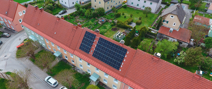 Das Happening-System, eine Kaskade aus Wärmepumpen, kommt in einem zusammenhängenden Riegel aus fünf Gebäuden in Liezen zum Einsatz. Heizzentrale und PV sind im beziehungsweise auf dem mittleren Gebäude installiert. Klein in weiß hinter dem Gebäude sind die Außeneinheiten der Luftwärmepumpen zu erkennen. Strombilanz und Anteil erneuerbarer Energien im Happening-Sys﻿tem. Beim Happening-­System liegen die Investitionskosten deutlich über dem Referenzsystem. Nach etwa 13 Jahren haben sich diese amortisiert.