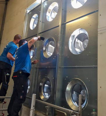 Optimierung einer RLT-Anlage bei einem Automobilhersteller in Berlin: Der Ventilator wurde zerlegt und mit einem Kran durch das Dach abtransportiert, das zuvor von einem Dachdecker geöffnet worden war. Anschließend wurde eine Ventilatorenwand („Fanwall“) als Grundkonstruktion zur Aufnahme energieeffizienter Ventilatoren mit EC-Motoren eingebaut.